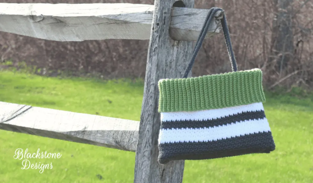 A crochet shoulder bag with stripes of white, grey, and green yarn.