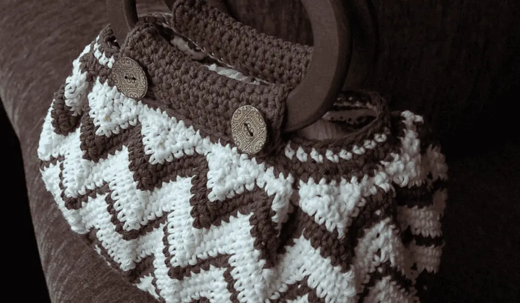 A crochet bag with brown zig zag accents on a mostly white bag.