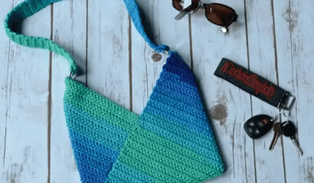 A crochet crossbody with a v-shape design. The yarn is a green and blue ombre color.