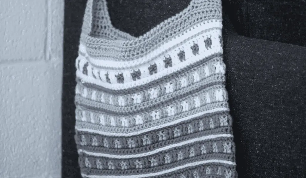 A grey crochet bag that keeps getting darker at each row towards the bottom with small stars of accent colors in each row.