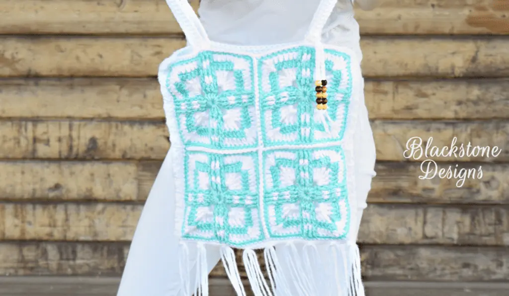 A crochet bag with four squares with blue lines and tassels on the bottom.