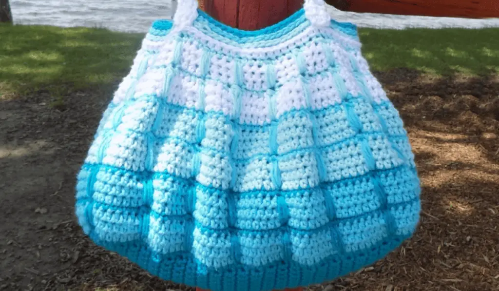 A crochet shoulder bag with rows of white, teal, light blue, and then a dark blue bottom.