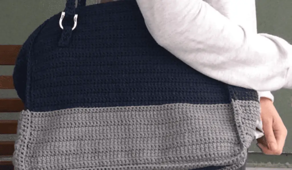 A crochet bag with dark blue top half and a grey bottom half. It's about the size of a small duffle bag.