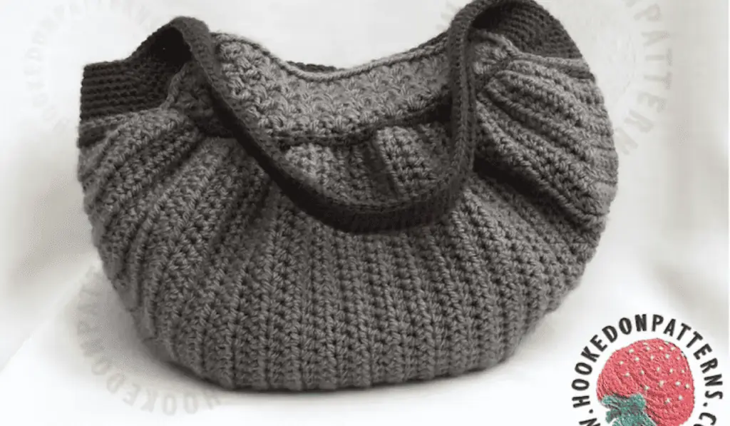 A grey crochet bag that is shaped in a half circle.