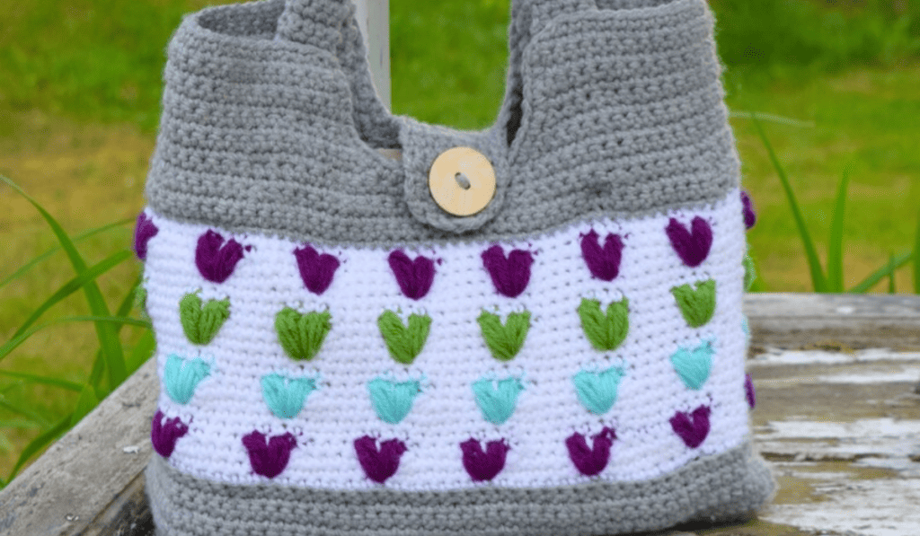 A crochet tote bag with multicolor heart detailings.