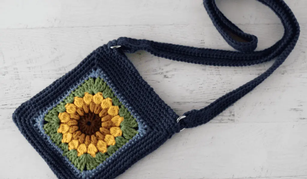 A small crochet crossbody bag with a sunflower deisgn on the side.