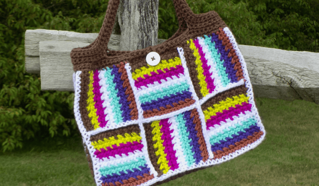 A crochet tote bag with multiple lines of colors, including brown, yellow, fushia, white, teal, purple, and brown.