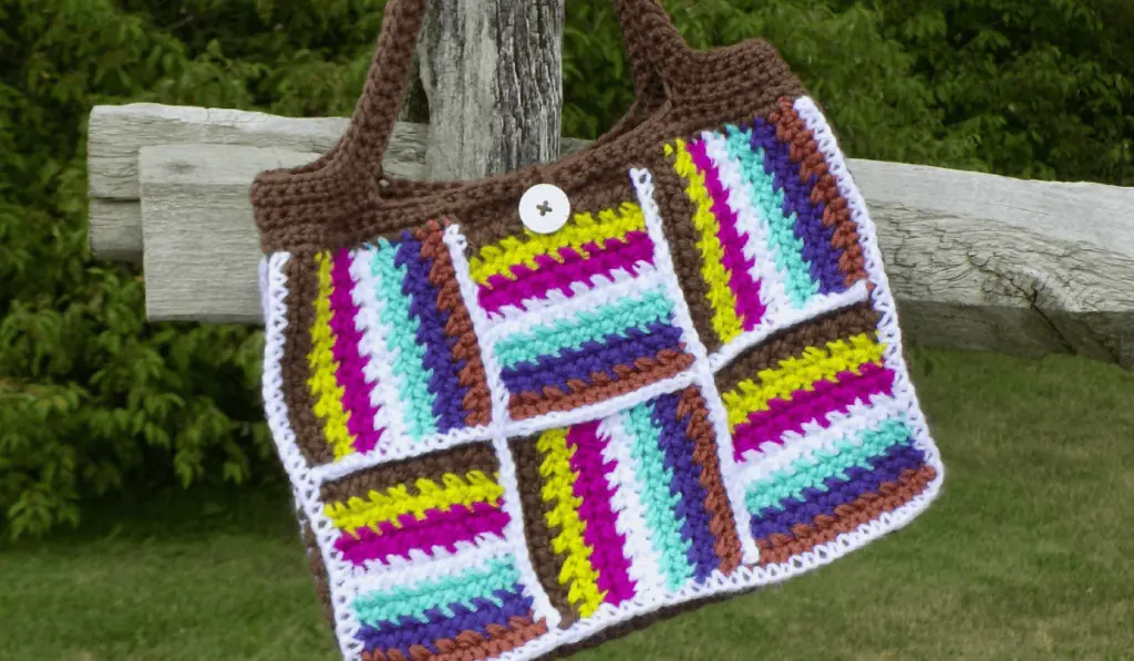 A crochet tote bag with multiple lines of colors, including brown, yellow, fushia, white, teal, purple, and brown.