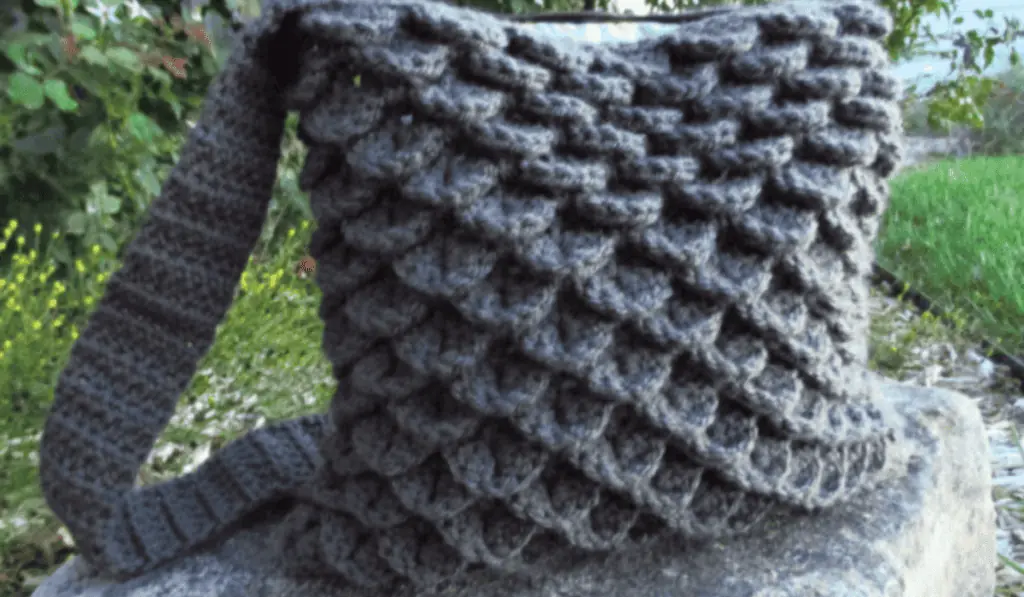 A crochet crossbody bag with a dragonscale design made out of all grey yarn.