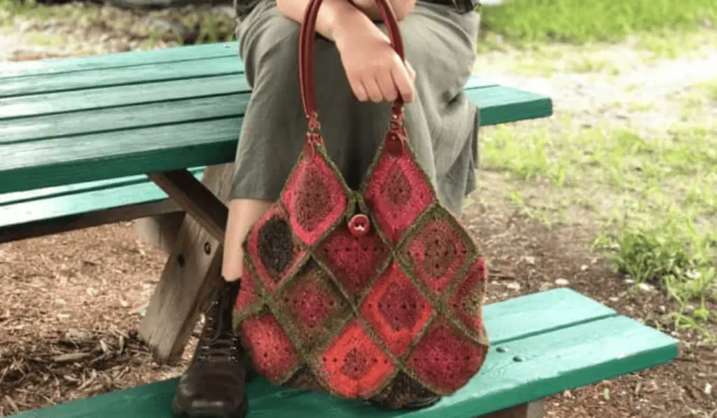 A boho crochet bag with reddish brown yarn and green joins.