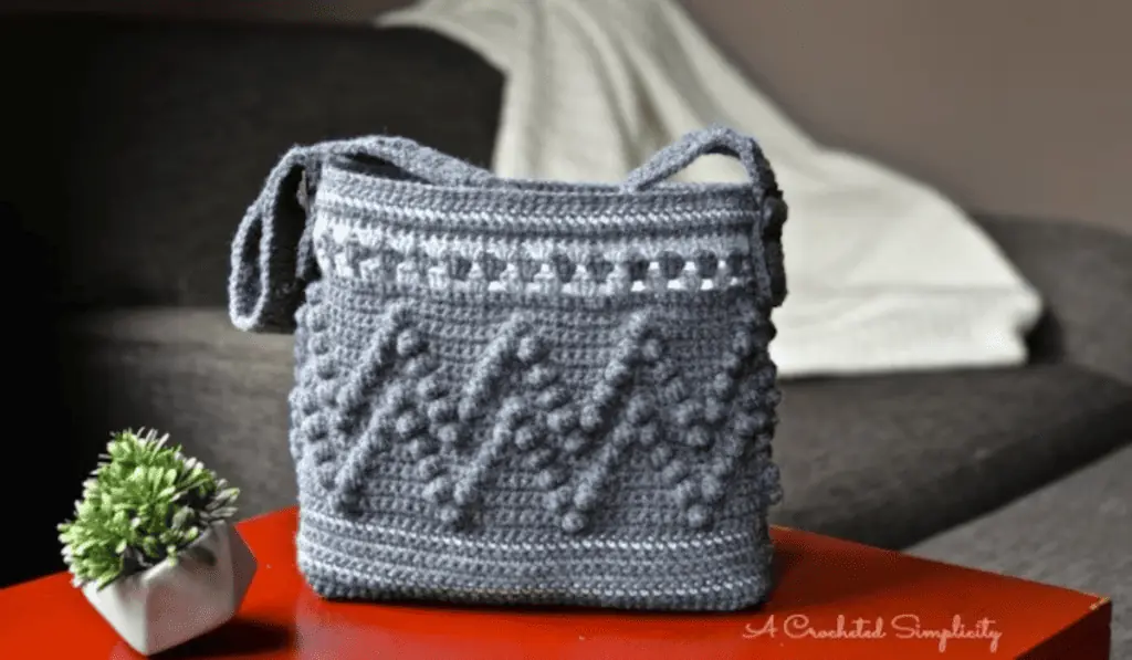 A grey crochet bag with a zigzag bobble stitch design.
