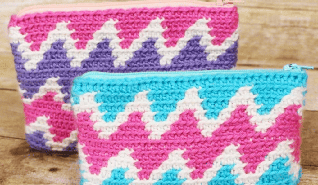 A zipper crochet pouch with blue, white, and pink yarn on one pouch and pink, white, and purple yarn on the other.