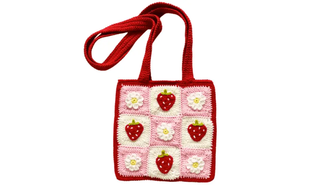 A crochet tote bag with interchange squares of strawberries and daisies.