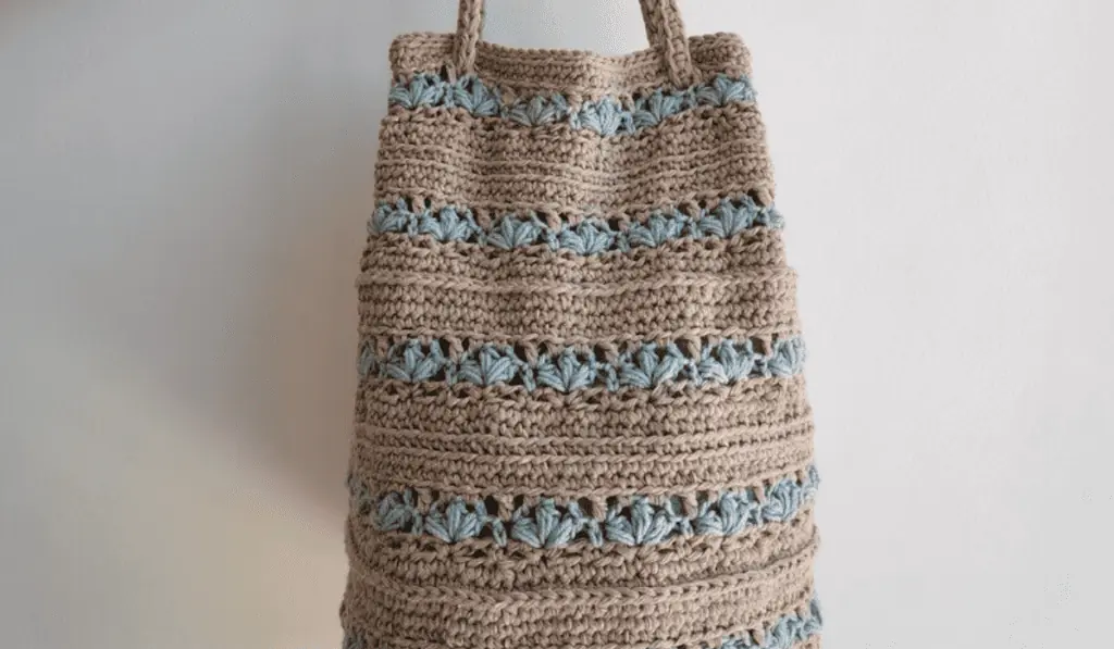 A brown crochet tote bag with rows of blue flowers every so often through the bag.