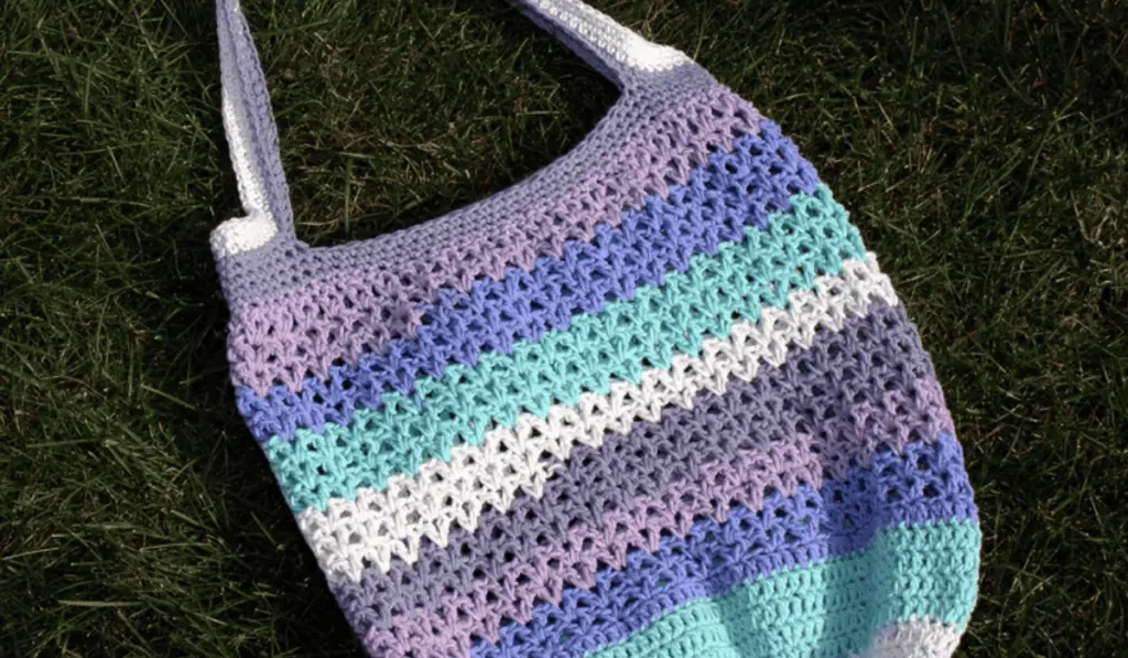 A crochet tote bag with stripes of purple, blue, and white yarn.
