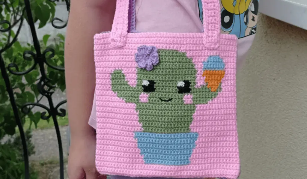 A pink crochet tote bag with a cactus design on the front.