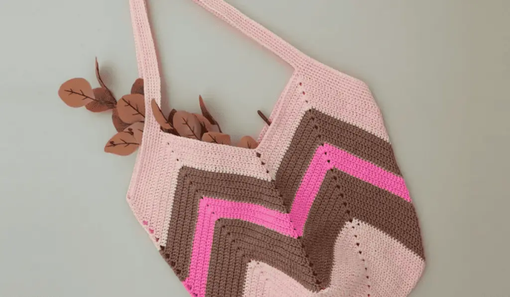 A crochet tote bag with zig-zag designs, the background is pink, with two rows of brown and a hot pink row.