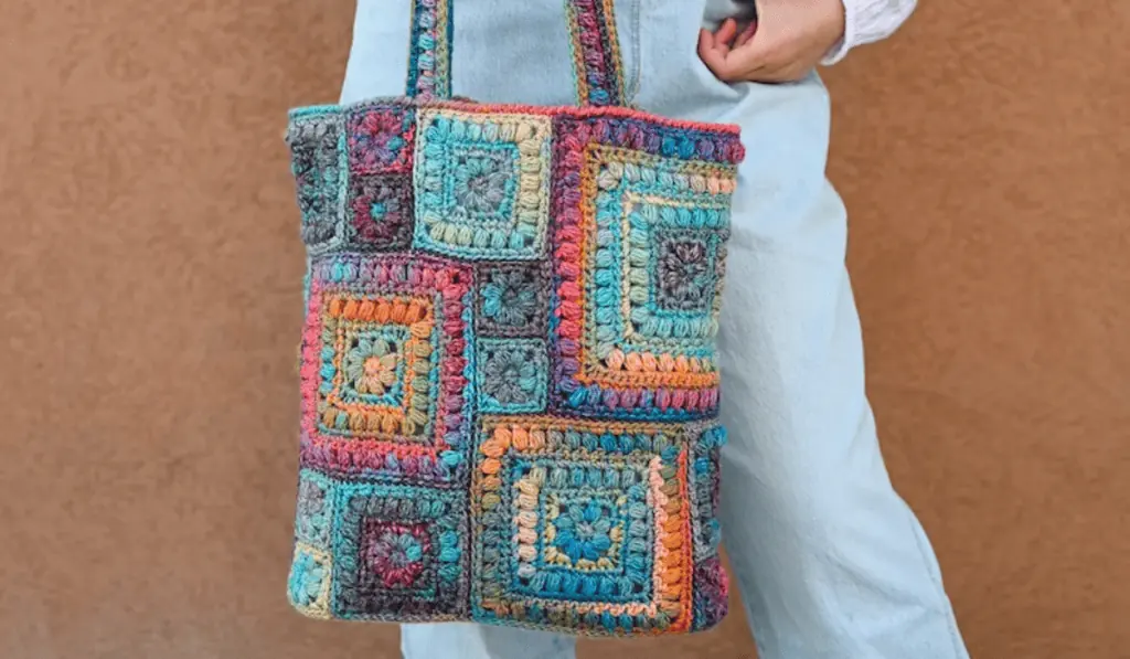 A crochet tote bag with multiple bright colors and many different sized squares.