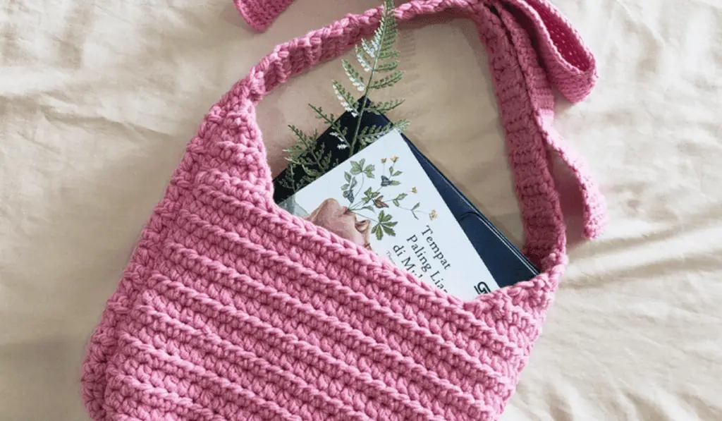 A pink crochet tote bag pattern with a large bow over the shoulder.