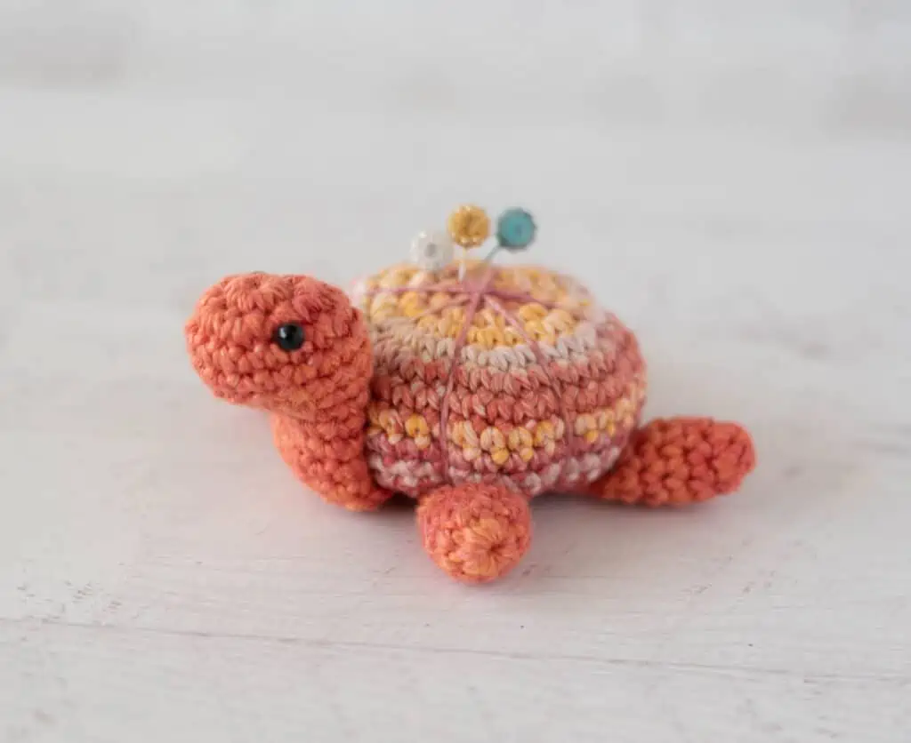Orange tone crochet turtle pincushion with floral decorative pins on top