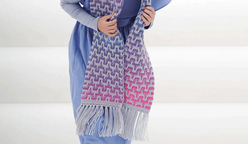 A beautiful ombre scarf with a pink, purple, and blue yarn background and grey detailing.