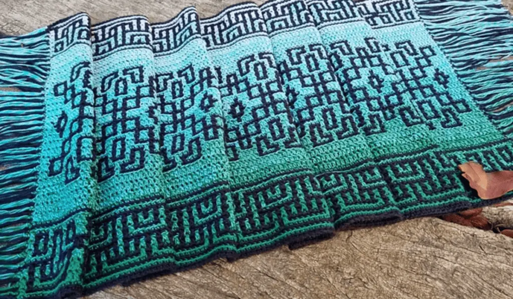 A mosaic table runner with a geometric design and a blue ombre yarn.