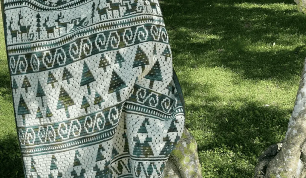 A mosaic crochet blanket pattern that features pine trees, reindeers with sleighs, and little Santas in green and white yarn.
