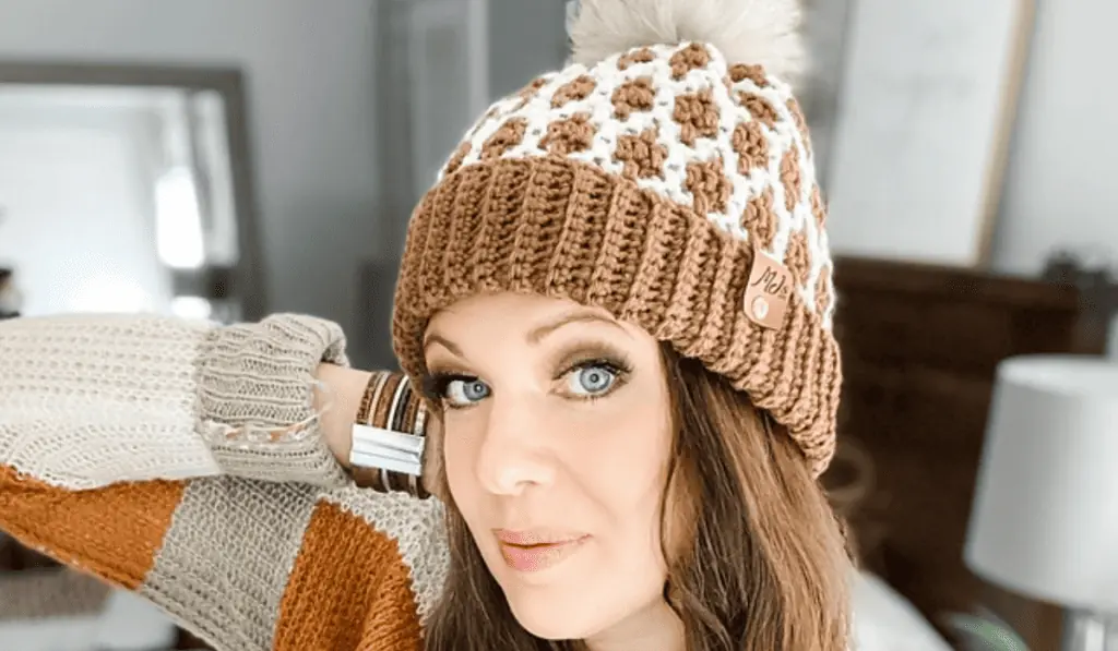 A mosaic crochet beanie with brown and white yarn and a little pom pom on the top.