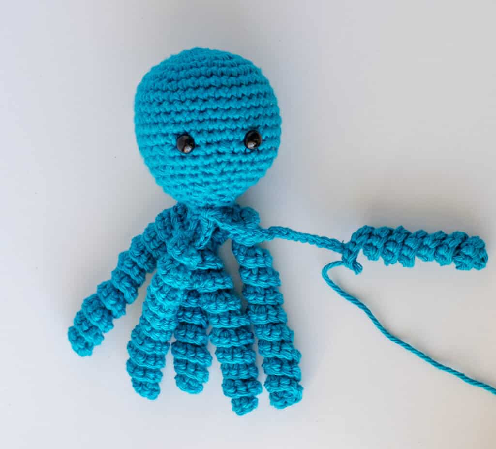 Bright blue crochet octopus with tentacle in progress