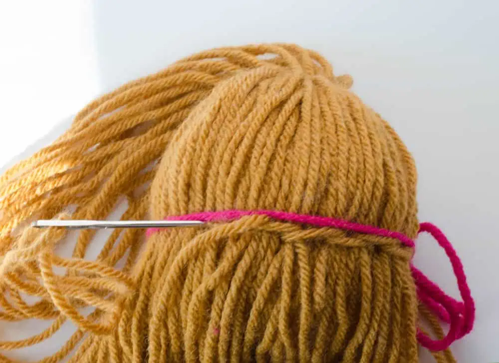 Close up of sewing hair down, gold yarn, yarn needle and pink yarn for example