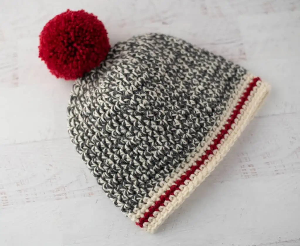 Crochet sock monkey hat in gray, cream and red yarn with red pom pom
