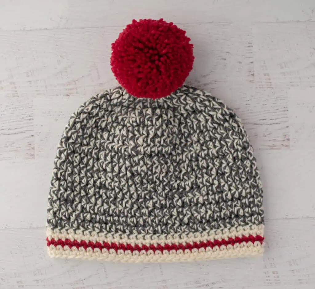 Crochet sock monkey hat in gray, cream and red yarn with red pom pom