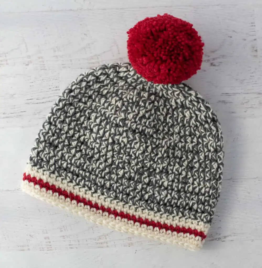 Crochet sock monkey hat in gray, cream and red yarn with red pom pom