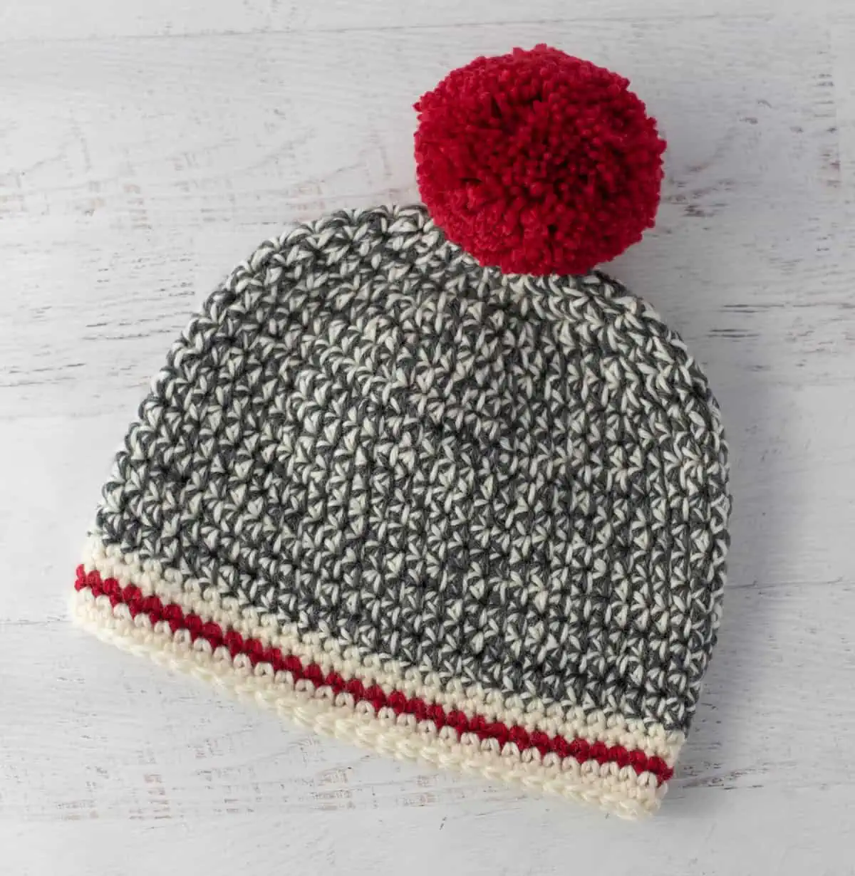 Crochet sock monkey hat in gray, cream and red yarn with red pom pom
