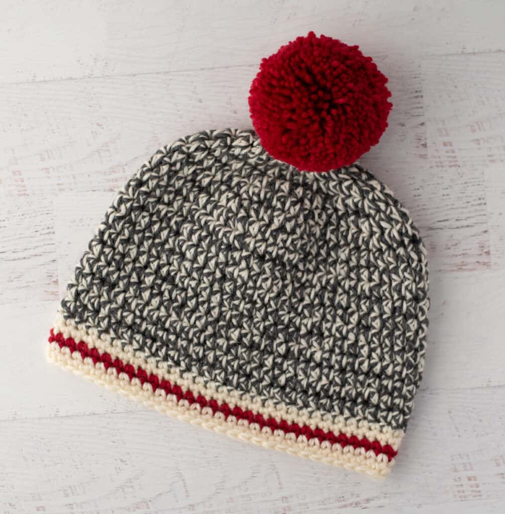 Crochet sock monkey hat in gray, cream and red yarn with red pom pom