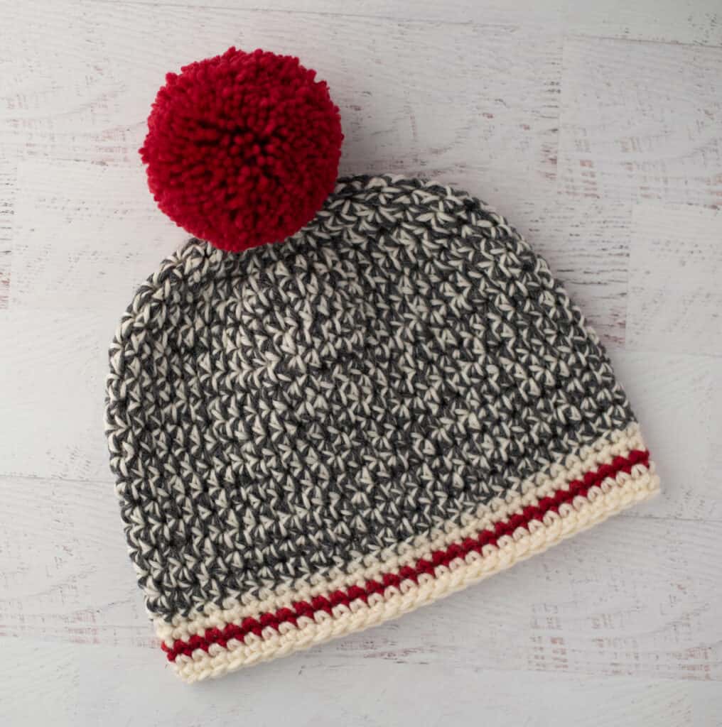 Crochet sock monkey hat in gray, cream and red yarn with red pom pom