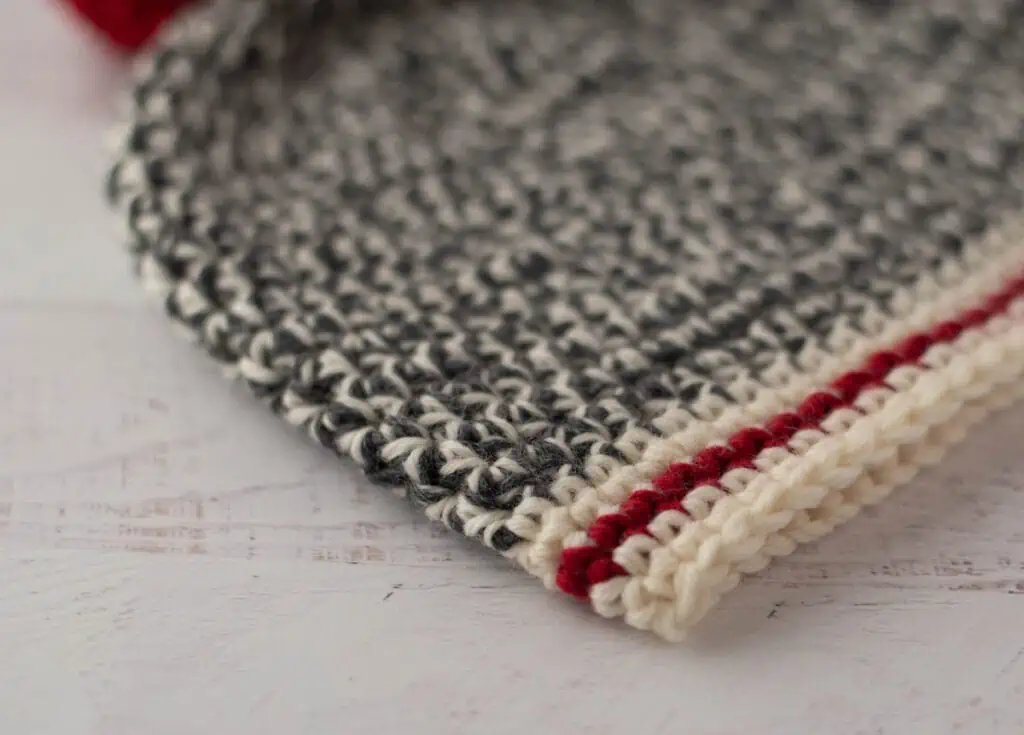 Crochet sock monkey hat in gray, cream and red yarn with red pom pom