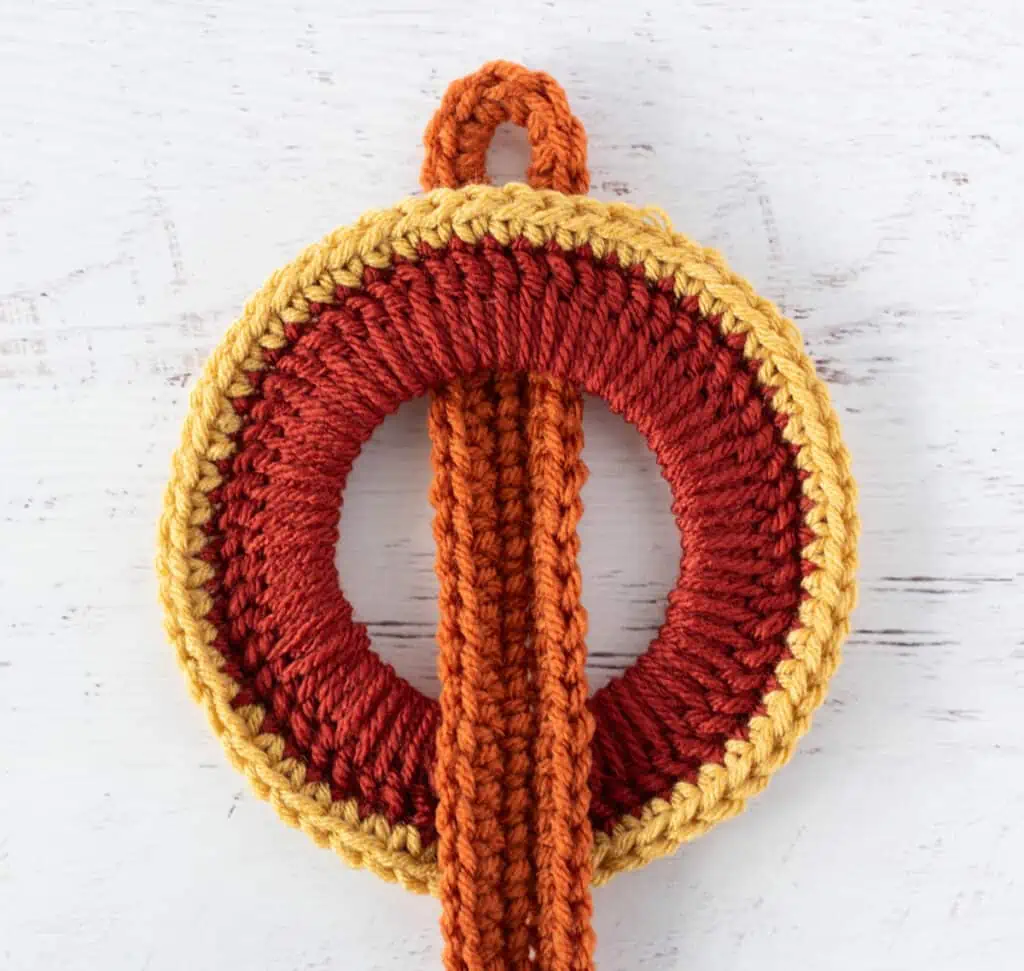 Orange crochet strap woven between orange crochet rings with yellow trim.