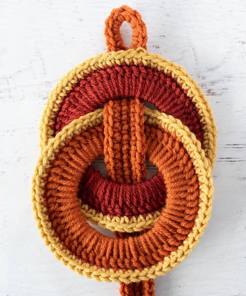 Orange crochet strap woven between orange crochet rings with yellow trim.