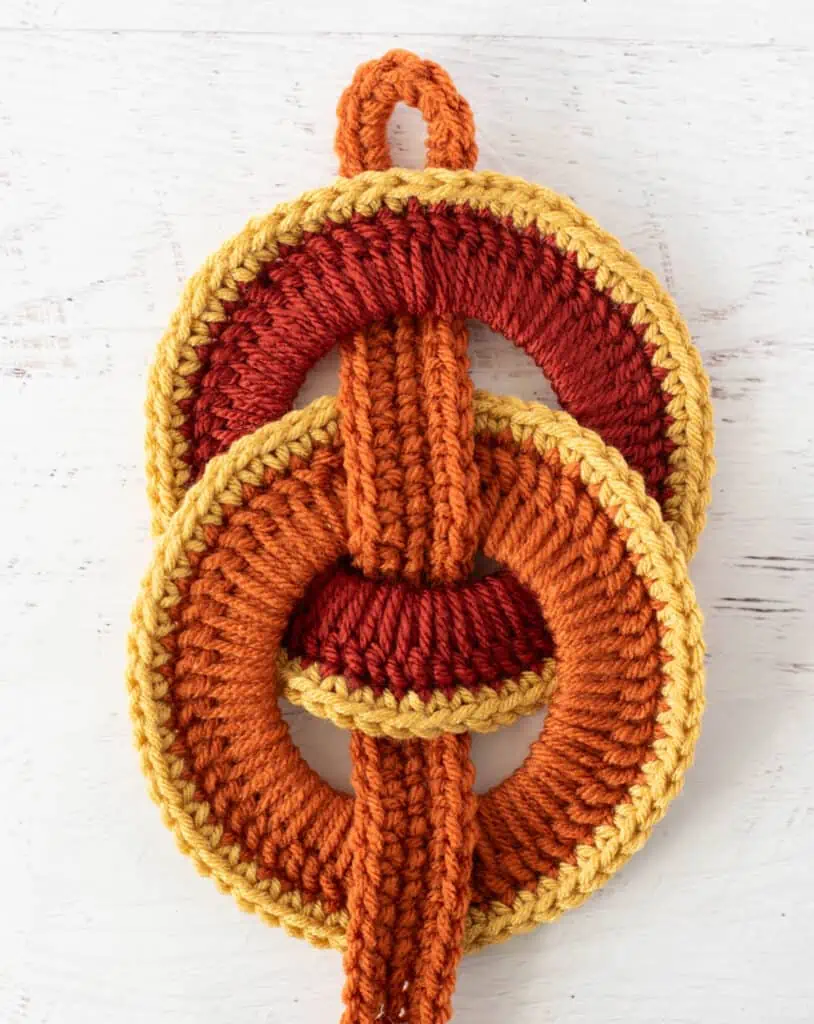 Orange crochet strap woven between orange crochet rings with yellow trim.