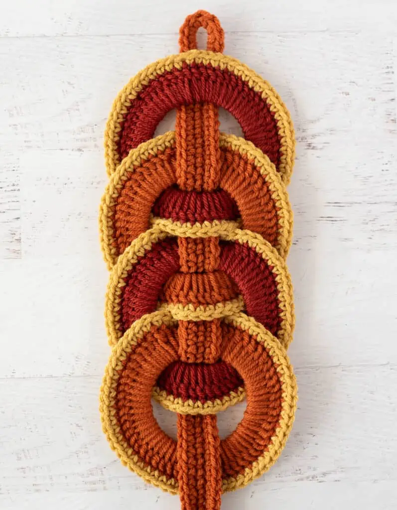 Orange crochet strap woven between orange crochet rings with yellow trim.