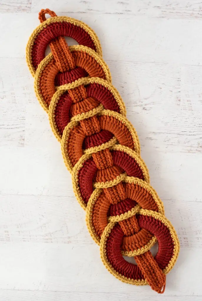 Orange crochet strap woven between orange crochet rings with yellow trim.