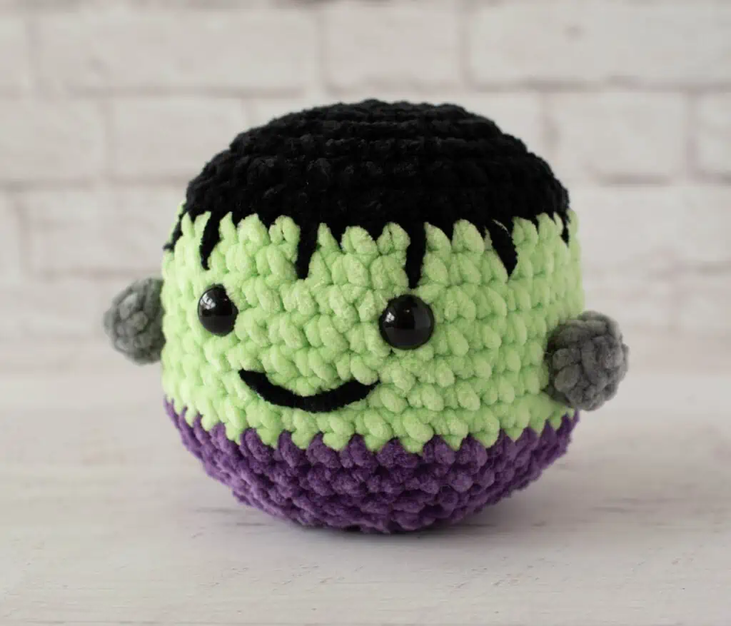 Stuffed Frankenstein monster with friendly smile made out of chenille yarn in black, green and purple