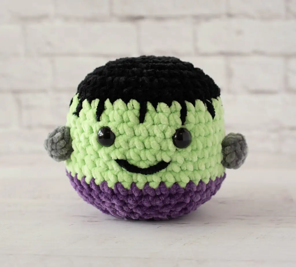 Stuffed Frankenstein monster with friendly smile made out of chenille yarn in black, green and purple