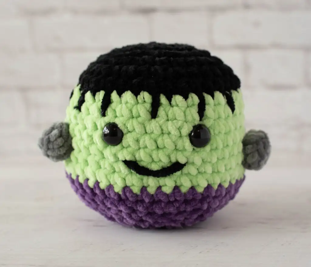 Stuffed Frankenstein monster with friendly smile made out of chenille yarn in black, green and purple