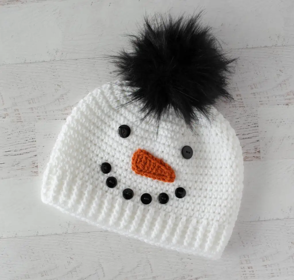 Crochet snowman hat with black buttons, orange carrot nose and black fur pom pom