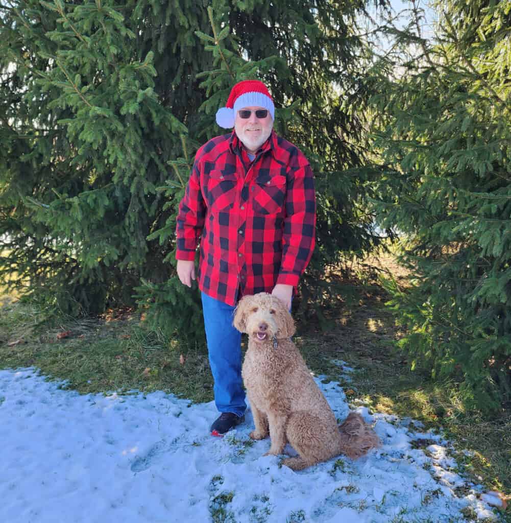 Man in red plaid shirt and crochet santa hat with dog