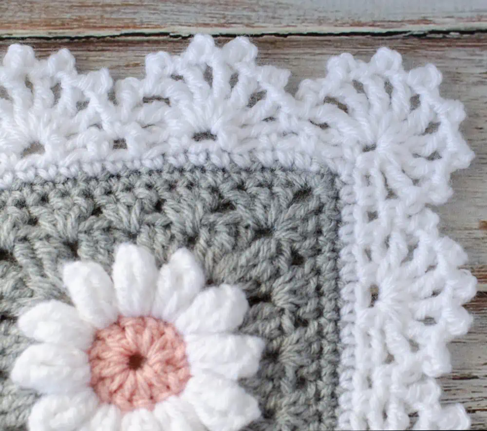 Corner of crochet daisy granny square afghan in gray, pink and white