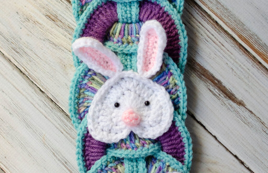 Up close image of crochet white bunny appliqué on blue and purple rings.