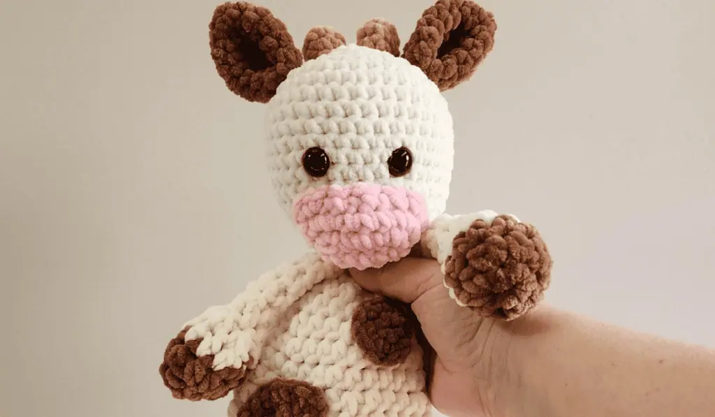 crochet cow snuggler made in cream, brown and pink chenille yarn.